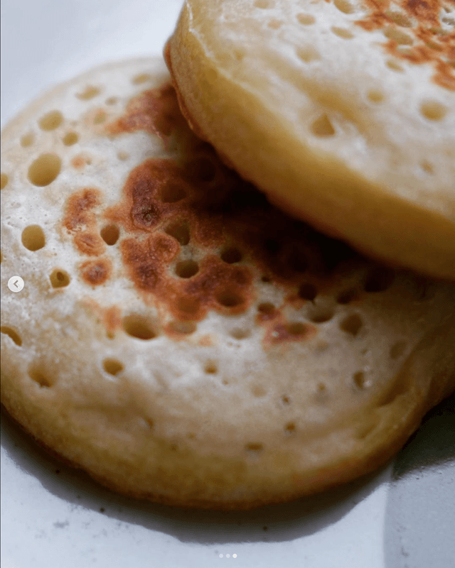 A close-up of two fluffy pancakes with golden-brown exteriors showcasing a lightly crisped texture and multiple small air pockets across the surface, stacked on a white plate.